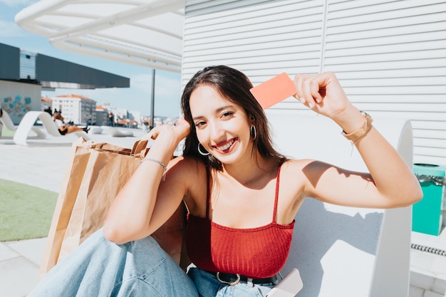 Jonge afrikaanse vrouw met een lege creditcardruimte die buiten winkelt met kopieerruimte. Gelukkig, trendy hipstermeisje dat online eten bestelt, kaartjes boekt tijdens een zonnige dag. Trendy jonge mensen