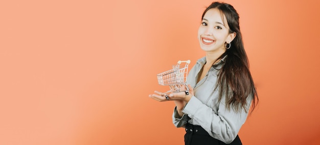 Jonge Afrikaanse vrouw met een winkelwagentje terwijl glimlachen naar de camera online kopen concept poseren geïsoleerd over oranje kleur muur achtergrond dagelijkse uitdrukkingen met kopie ruimte in studio