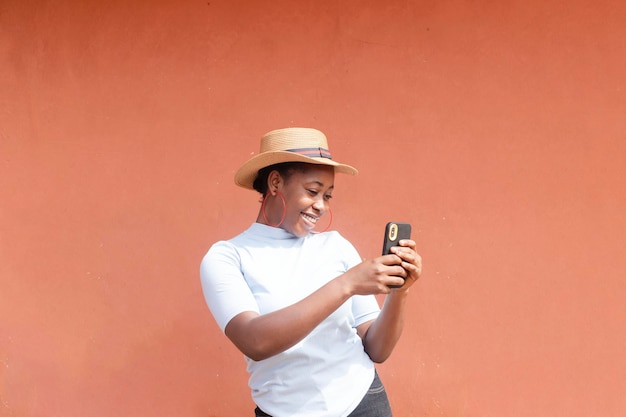 Jonge afrikaanse vrouwelijke blogger houdt een mobiele telefoon omhoog die lacht terwijl hij een camera-selfie maakt