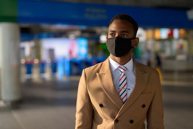 Jonge Afrikaanse zakenman die met masker denkt voor bescherming tegen de uitbraak van coronavirus bij het skytrain-station