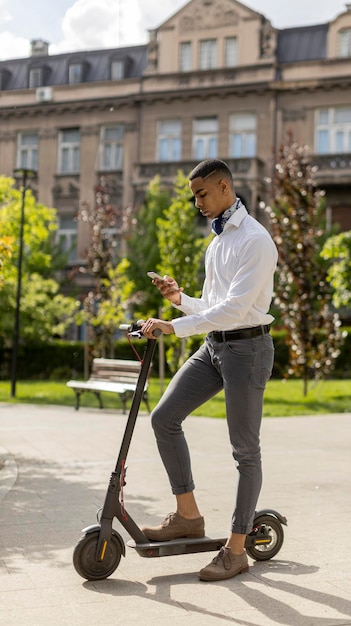 Jonge Afro-Amerikaan die mobiele telefoon gebruikt terwijl hij met een elektrische scooter op straat staat