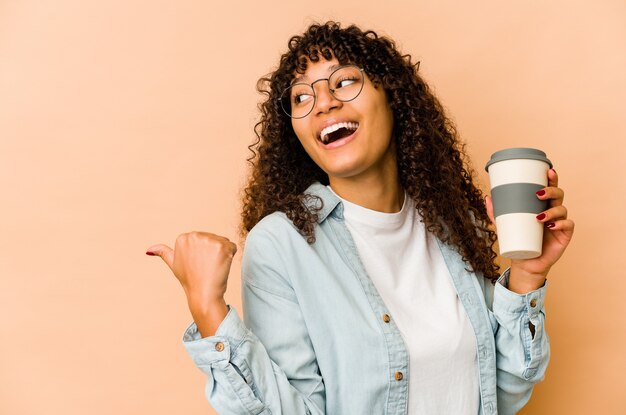 Jonge afro-amerikaanse afrovrouw die een afhaalkoffie houdt wijst met duimvinger weg, lachend en zorgeloos.