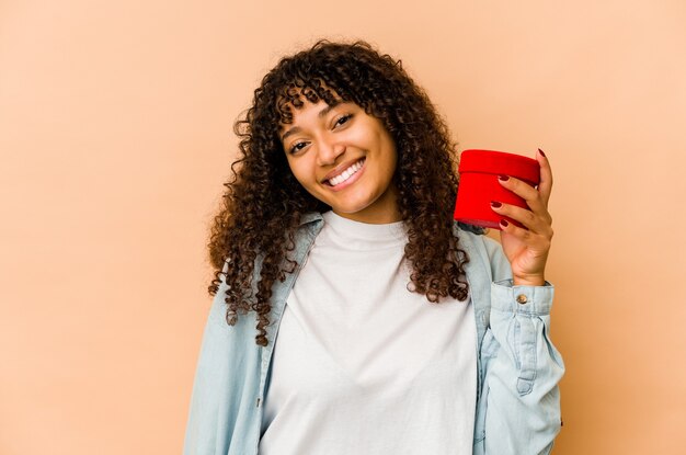 Jonge afro-amerikaanse afrovrouw die een gelukkige, glimlachende en vrolijke gift van de valentijnskaartendag houdt.