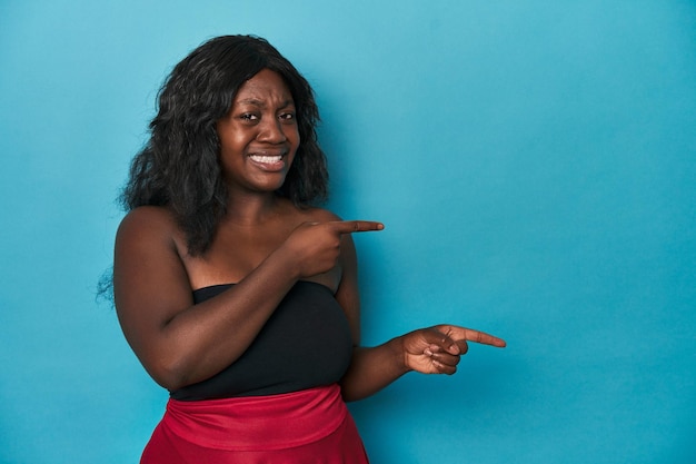 Jonge afro-amerikaanse bochtige vrouw geschokt wijzend met wijsvingers naar een kopieerruimte