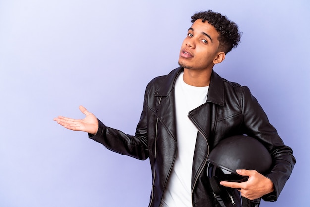 Jonge Afro-Amerikaanse curly biker man geïsoleerd met een kopie ruimte op een palm en met een andere hand op de taille.