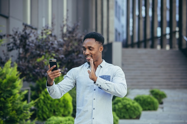 Jonge Afro-Amerikaanse freelancer praten over video-oproep in de buurt van kantoor vrolijk lachende man