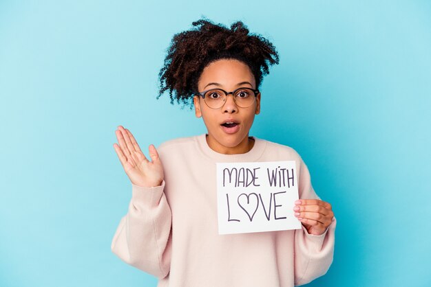 Jonge Afro-Amerikaanse gemengd ras vrouw met een gemaakt met liefde concept verrast en geschokt.