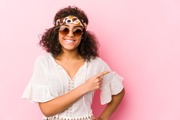 Jonge Afro-Amerikaanse hipster vrouw geïsoleerd op roze glimlachend en opzij wijst