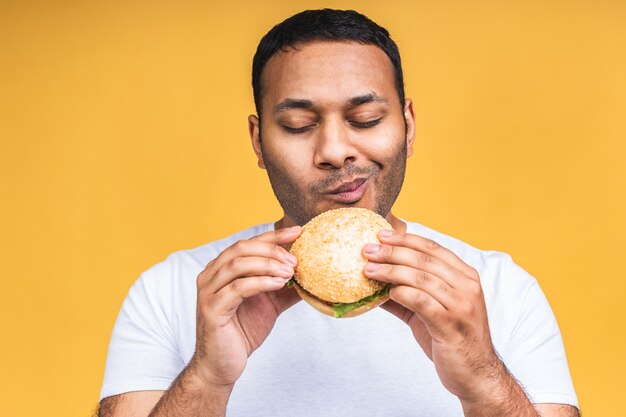 Jonge afro-amerikaanse indiase zwarte man eten hamburger geïsoleerd op gele achtergrond. dieet concept.