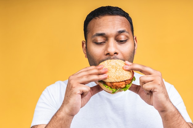 Jonge Afro-Amerikaanse Indiase zwarte man eten hamburger geïsoleerd op gele achtergrond. Dieet concept.