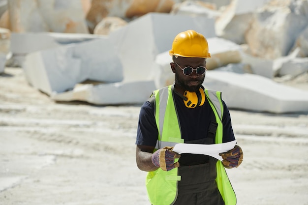 Jonge afro-amerikaanse ingenieur in handschoenen, veiligheidshelm uniform en zonder bril