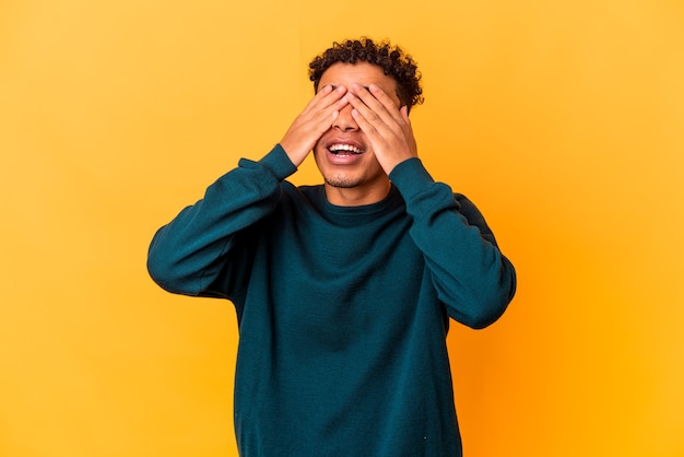 Jonge Afro-Amerikaanse krullende man geïsoleerd op paars heeft betrekking op ogen met handen, glimlacht in het algemeen wachtend op een verrassing.