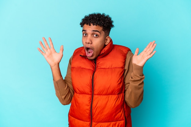 Jonge Afro-Amerikaanse krullende man op blauw verrast en geschokt.