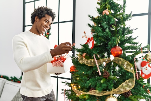 Jonge afro-amerikaanse man die lacht gelukkig kerstboom thuis versieren.