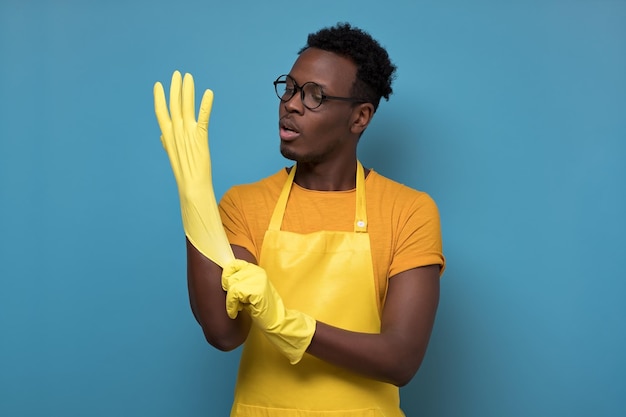 Jonge afro-amerikaanse man die schoonmaakt met handschoenen die op de gele muur staan