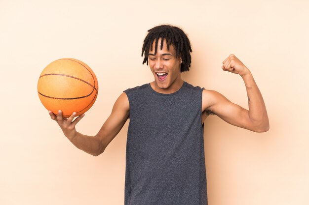 Jonge Afro-Amerikaanse man geïsoleerd op beige muur spelen basketbal