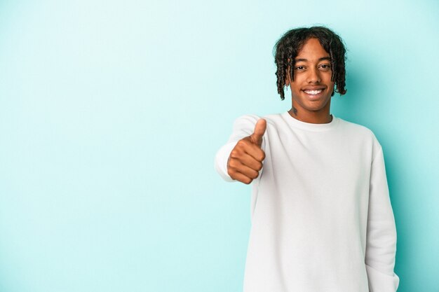 Jonge Afro-Amerikaanse man geïsoleerd op blauwe achtergrond glimlachend en duim omhoog