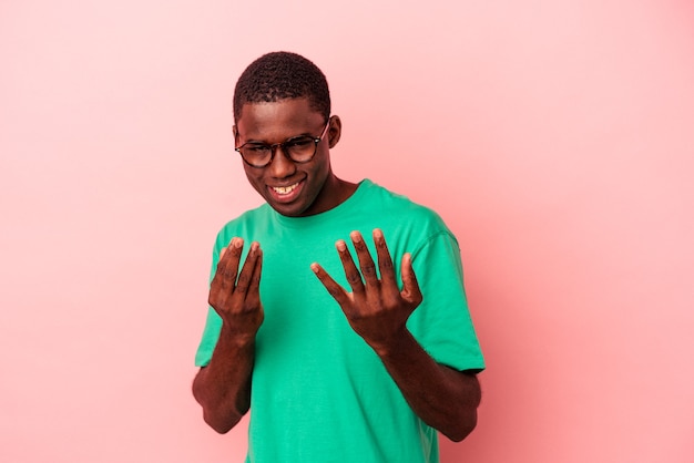 Jonge Afro-Amerikaanse man geïsoleerd op een roze achtergrond die met de vinger naar je wijst alsof uitnodigend dichterbij komt.