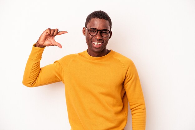 Jonge Afro-Amerikaanse man geïsoleerd op een witte achtergrond met iets kleins met wijsvingers, glimlachend en zelfverzekerd.