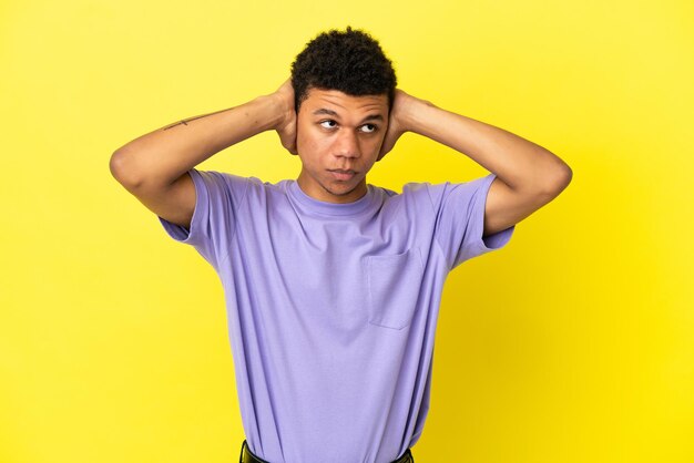 Jonge Afro-Amerikaanse man geïsoleerd op gele achtergrond gefrustreerd en oren bedekt
