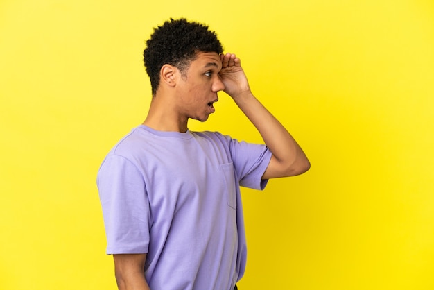 Jonge Afro-Amerikaanse man geïsoleerd op gele achtergrond met verrassingsuitdrukking terwijl hij opzij kijkt