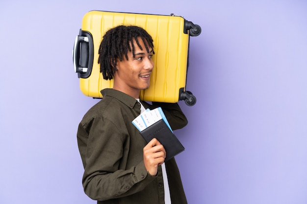 Jonge Afro-Amerikaanse man geïsoleerd op paars in vakantie met koffer en paspoort