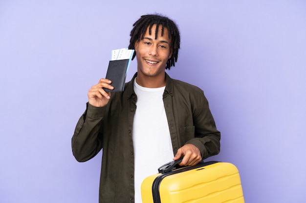 Jonge Afro-Amerikaanse man geïsoleerd op paarse achtergrond in vakantie met koffer en paspoort
