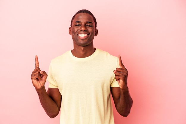 Jonge Afro-Amerikaanse man geïsoleerd op roze achtergrond geeft aan dat met beide voorvingers een lege ruimte wordt weergegeven