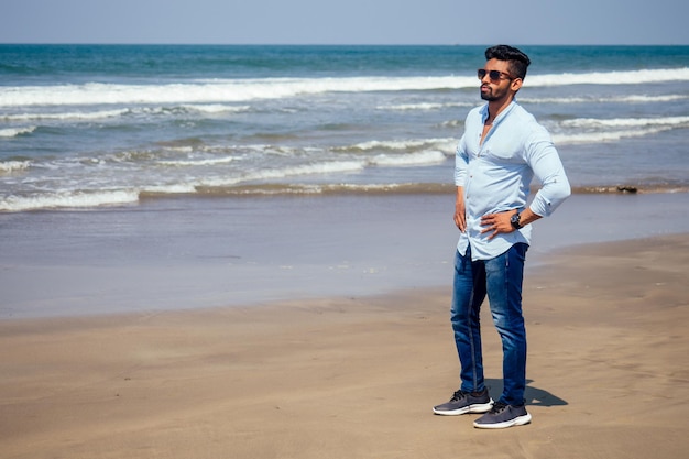 Jonge Afro-Amerikaanse man in blauw shirt en spijkerbroek op het oceaanstrand.