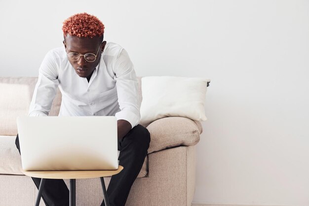 Jonge Afro-Amerikaanse man in formele kleding zit binnenshuis met laptop in handen