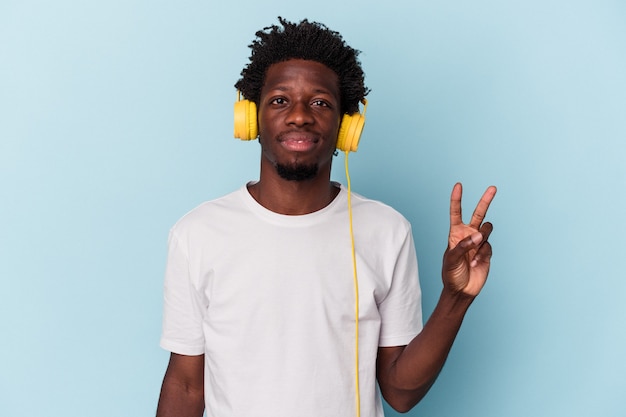 Jonge Afro-Amerikaanse man luisteren naar muziek geïsoleerd op blauwe achtergrond met nummer twee met vingers.