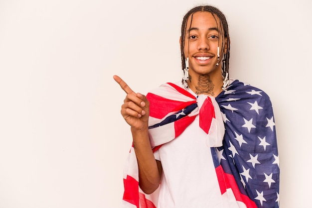 Jonge Afro-Amerikaanse man met een Amerikaanse vlag geïsoleerd op een witte achtergrond glimlachend en opzij wijzend met iets op lege ruimte
