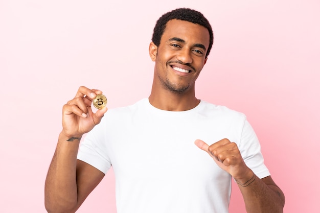 Jonge Afro-Amerikaanse man met een Bitcoin over geïsoleerde roze achtergrond, trots en zelfvoldaan