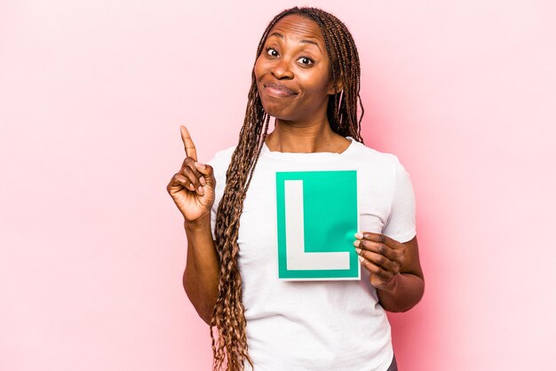 Jonge Afro-Amerikaanse man met een bord voor beginnersbestuurders dat op roze achtergrond wordt geïsoleerd