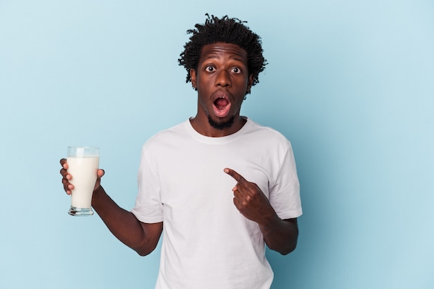 Jonge afro-amerikaanse man met een glas melk geïsoleerd op een blauwe achtergrond die naar de zijkant wijst