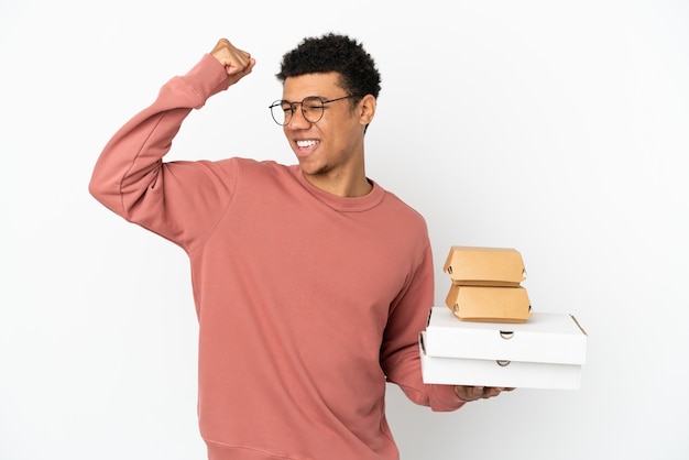Jonge Afro-Amerikaanse man met een hamburger en pizza's geïsoleerd op een witte achtergrond die een overwinning viert