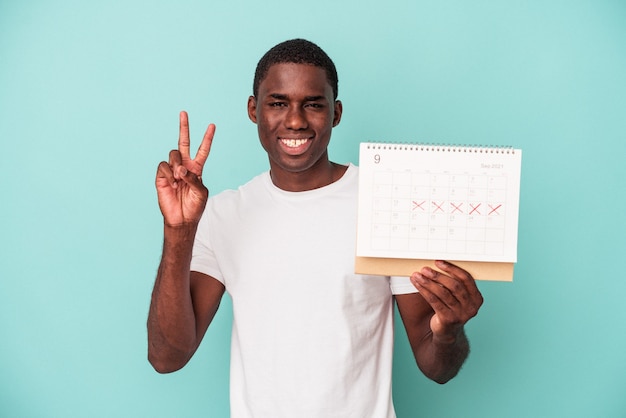 Jonge Afro-Amerikaanse man met een kalender geïsoleerd op een blauwe achtergrond met nummer twee met vingers.