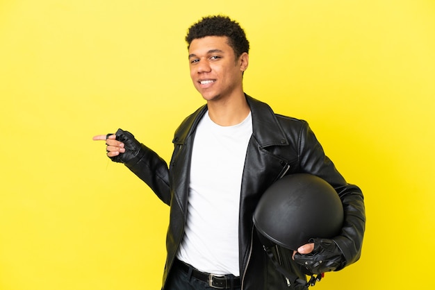 Jonge Afro-Amerikaanse man met een motorhelm geïsoleerd op een gele achtergrond wijzende vinger naar de zijkant