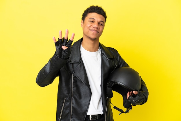 Jonge Afro-Amerikaanse man met een motorhelm geïsoleerd op gele achtergrond gelukkig en vier tellen met vingers