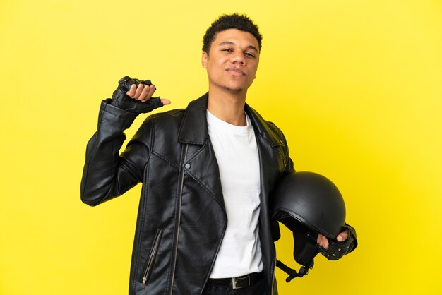 Jonge Afro-Amerikaanse man met een motorhelm geïsoleerd op gele achtergrond trots en zelfvoldaan