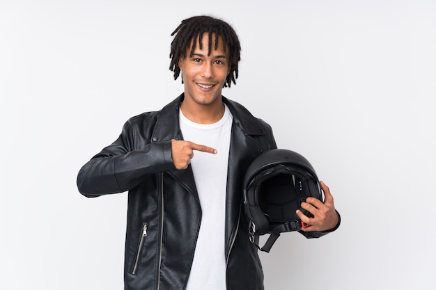 Jonge Afro-Amerikaanse man met een motorhelm op witte muur en wijst het