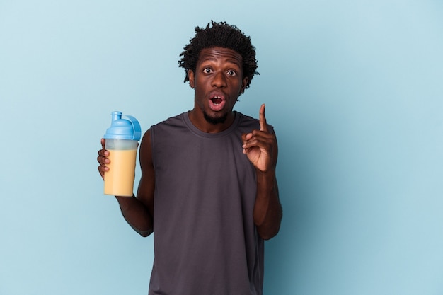 Jonge Afro-Amerikaanse man met eiwit milkshake geïsoleerd op blauwe achtergrond met een idee, inspiratie concept.