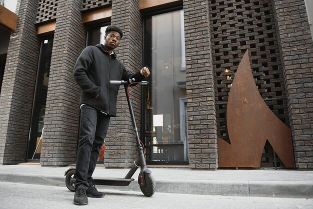 Jonge Afro-Amerikaanse man met elektrische scooter in de stad