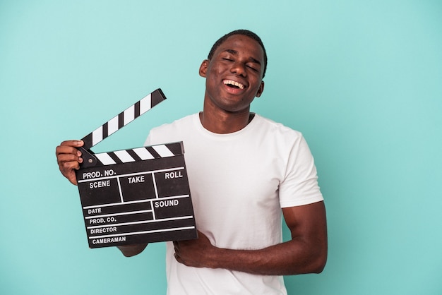 Jonge Afro-Amerikaanse man met Filmklapper geïsoleerd op blauwe achtergrond lachen en plezier hebben.