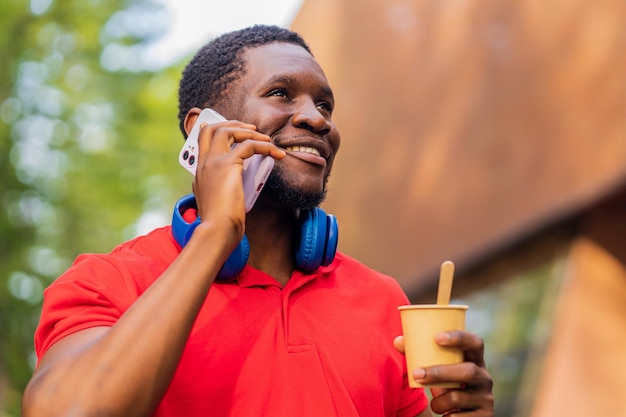 Jonge Afro-Amerikaanse man met koptelefoon op nek met smartphone in zomerpark