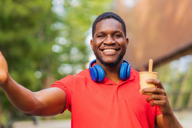 Jonge Afro-Amerikaanse man met koptelefoon op nek met smartphone in zomerpark