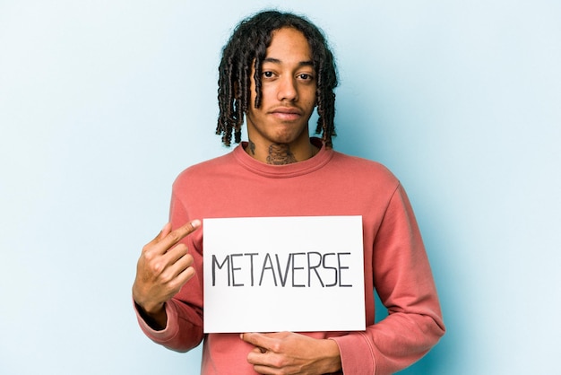 Jonge Afro-Amerikaanse man met metaverse plakkaat geïsoleerd op een blauwe achtergrond en met de vinger naar je wijzend alsof je dichterbij komt