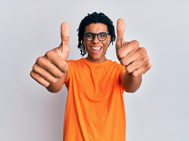 Jonge afro-amerikaanse man met vrijetijdskleding en bril die positief gebaar met de hand goedkeurt, duimen omhoog glimlachend en blij voor succes. winnaar gebaar.