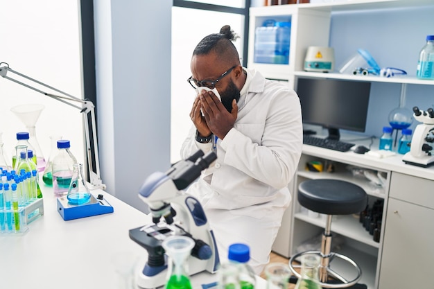 Jonge afro-amerikaanse man met wetenschapper uniforme ziekte met behulp van servet in het laboratorium