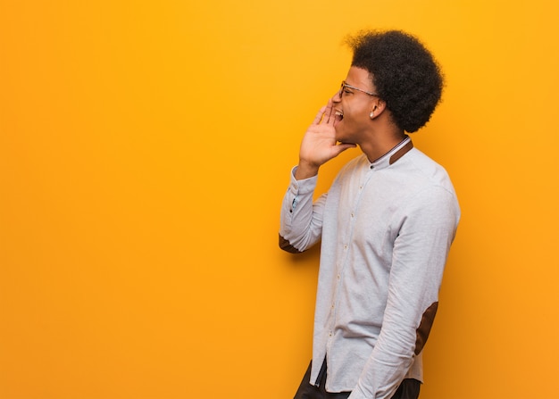 Jonge afro-amerikaanse man over een oranje muur fluisteren roddel ondertoon